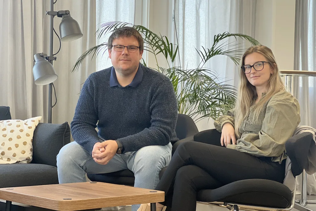 Kristoffer och Felicia sitter i varsin fåtölj och tittar in i kameran. Kristoffer har kort, brunt hår och glasögon. Han bär ljusa jeans och en mörkblå tröja. Felicia har långt mörkblont hår och glasögon. Hon bär en grön tunika och svarta byxor.